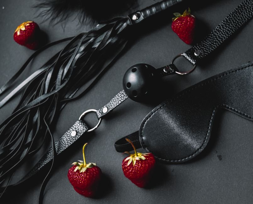 Accessoires de jeux kinky posés à plat sur fond sombre avec des fraises