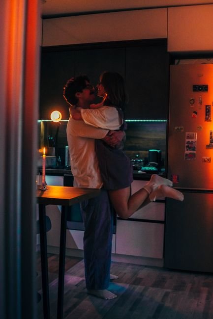 Couple s'enlaçant avec fougue dans une cuisine éclairée à la bougie