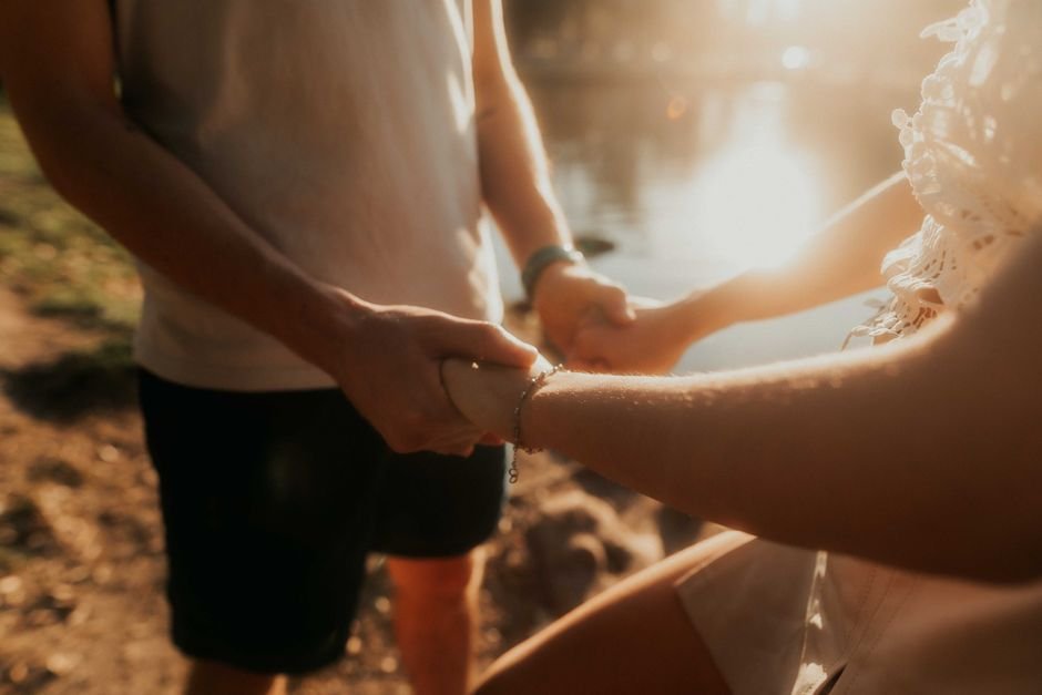 Couple se tenant les mains au bord d’un lac au soleil couchant