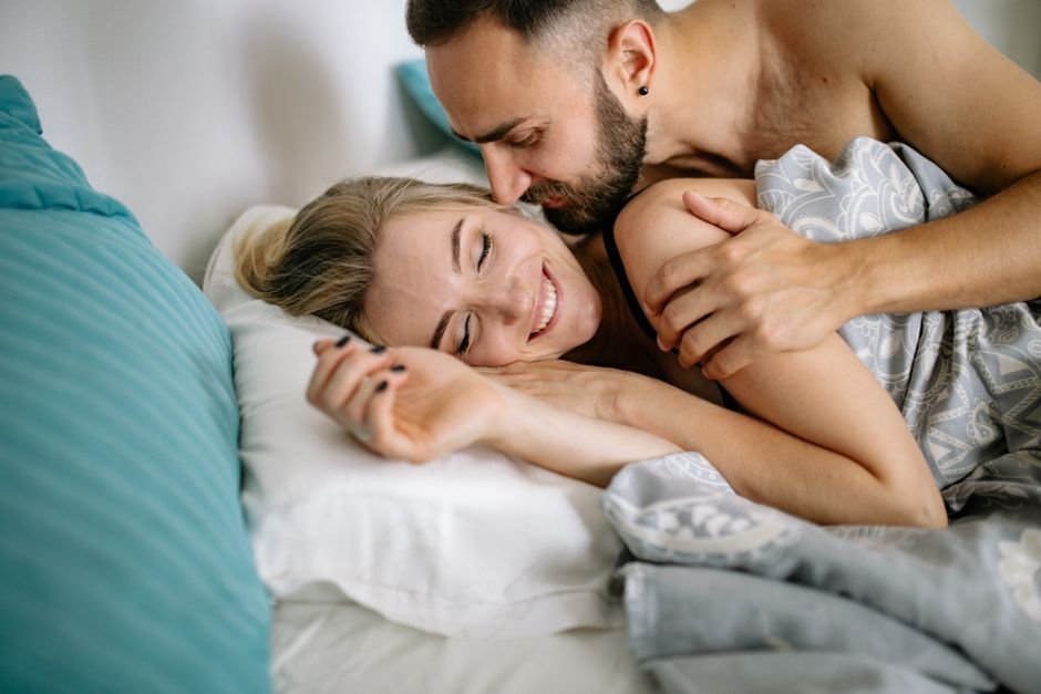 Couple souriant et enlacé au lit lors d’un moment tendre