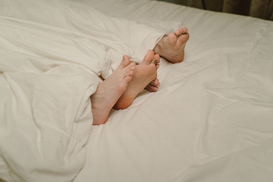 Deux paires de pieds dépassant d’un drap blanc, couple au lit
