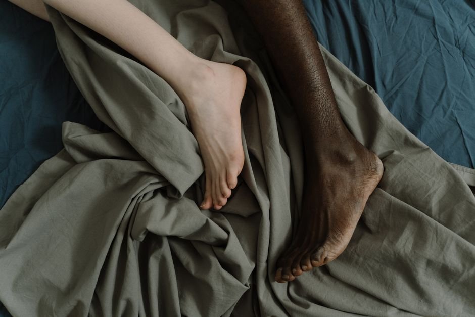 Deux pieds enlacés d’un couple sur des draps froissés, évoquant l’intimité