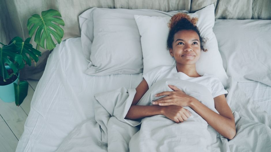 Femme détendue et souriante allongée dans un lit, illustrant le lâcher-prise