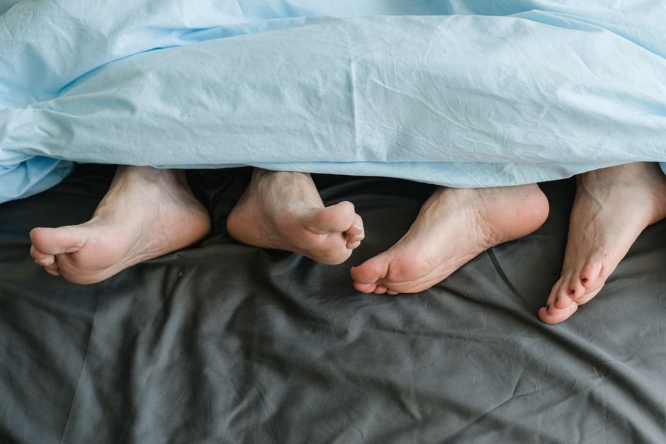Pieds de deux personnes côte à côte sous une couette